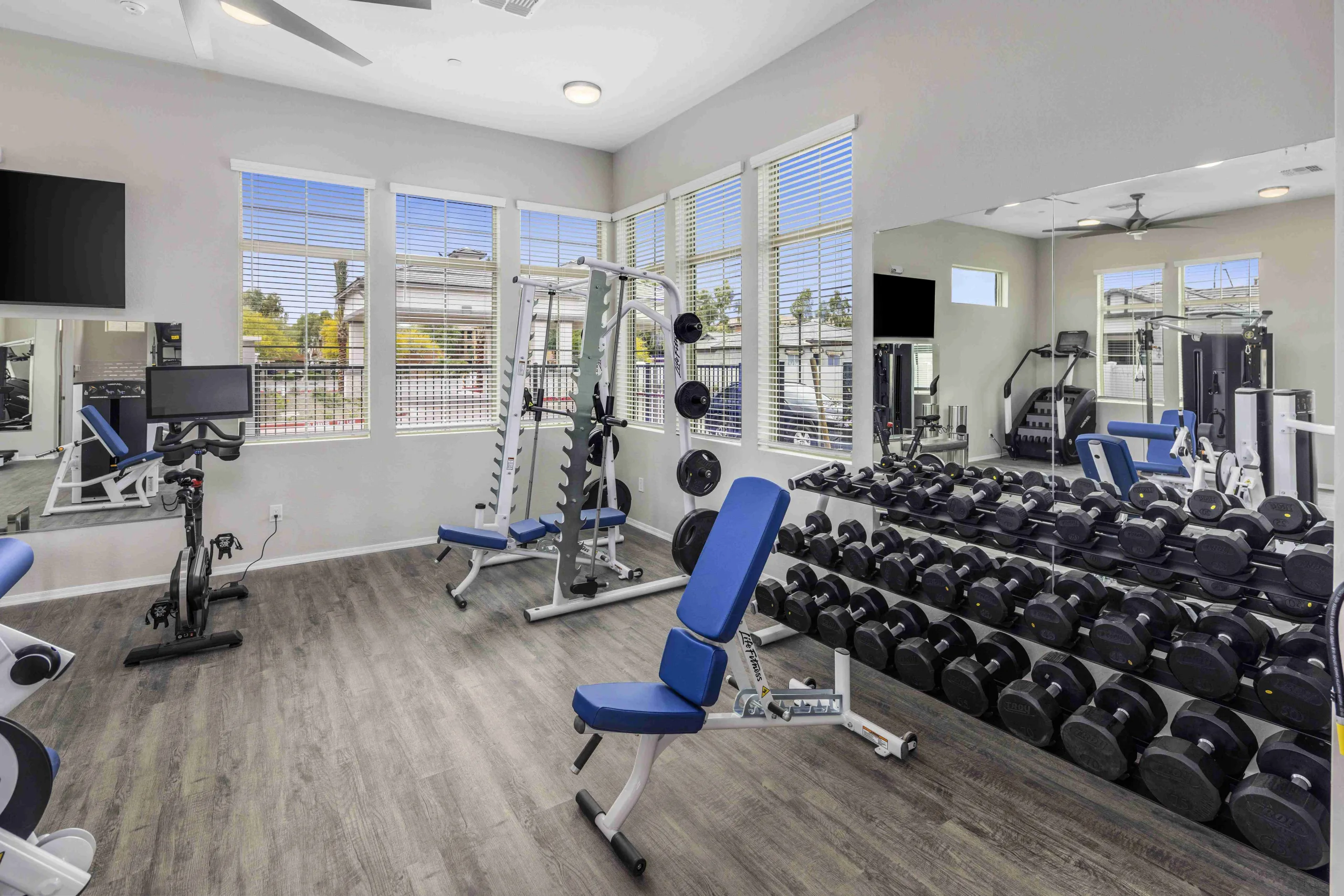Fitness studio with a weight rack and mirrors, assisted workout machines with adjustable weights, a stair climber, bench, elliptical, bike, and treadmill.