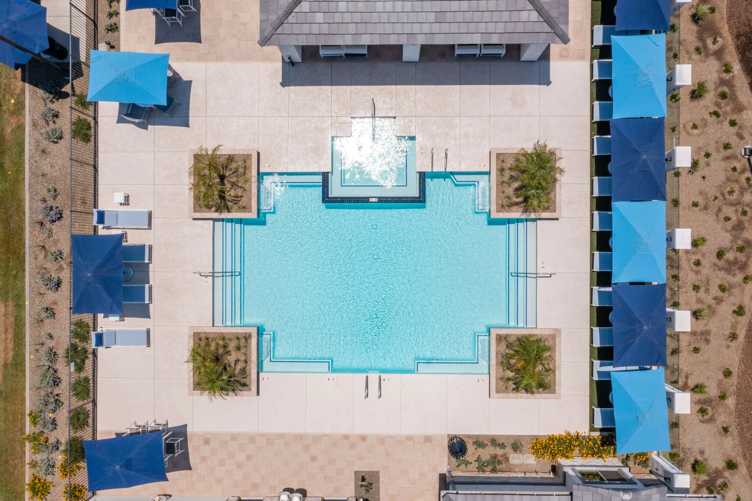 Aerial view of pool and spa deck with water features, outdoor covered pergola, and lawn chairs on grass.